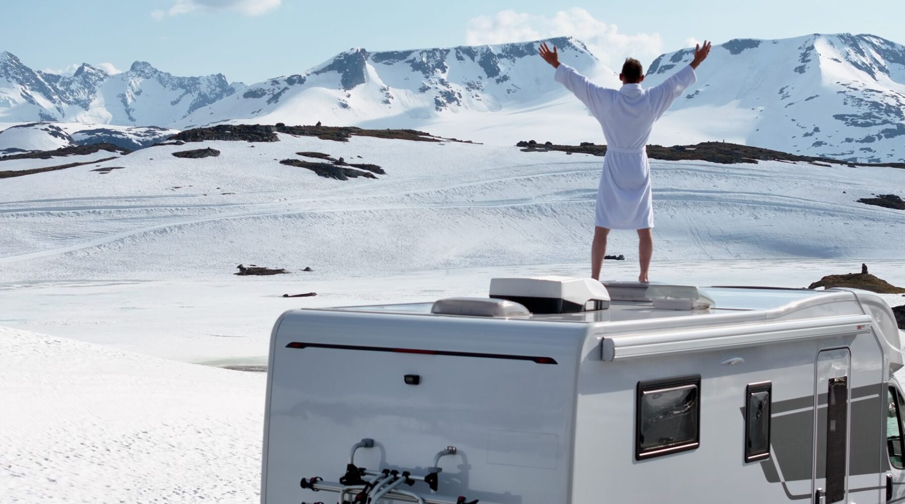 Man with his arms raised on the roof of a camper van in snowy mountains